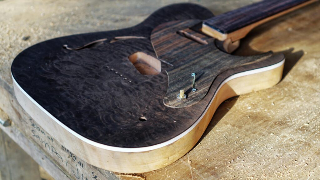 Close-up of a handcrafted electric guitar body on a wooden workbench, highlighting woodwork detail.